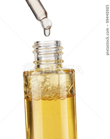 Part of a bottle with yellow cosmetic serum. Cosmetic glass pipette with a yellow oily drop of serum close-up on a white background. 99448985
