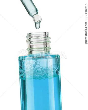 Part of a bottle with blue cosmetic serum. Cosmetic glass pipette with a blue oily drop of serum close-up on a white background. 99448986