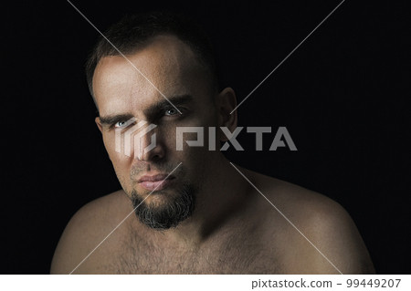 A dramatic portrait of a handsome man in an unobtrusive setting. Close up of a handsome bearded man with no clothes on a black background. Sexy man looking into the camera. A dramatic portrait of a handsome man in an unobtrusive setting. Close up of a handsome bearded man with no clothes on a black background. Sexy man looking into the camera. 99449207
