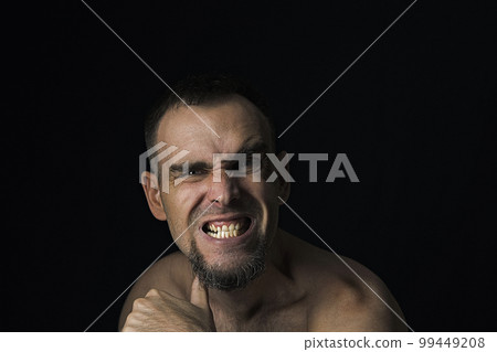 A Caucasian man without a shirt is threatening with his thumb at his throat. Portrait of an aggressive man on a black background. A Caucasian man without a shirt is threatening with his thumb at his throat. Portrait of an aggressive man on a black background. 99449208