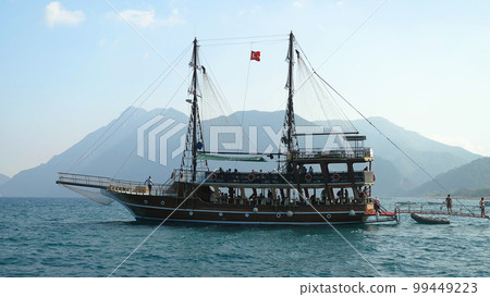 A beautiful harbour with a lonely tourist boat. View of a sunny harbour with a lonely wooden tourist boat at anchor. Blue sky and mountains in the background. A beautiful harbour with a lonely tourist boat. View of a sunny harbour with a lonely wooden tourist boat at anchor. Blue sky and mountains in the background. 99449223