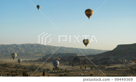 Colorful balloons flying over the mountainous landscape of Cappadocia. A popular tourist spot. Hot air balloons at dawn. Colorful balloons flying over the mountainous landscape of Cappadocia. A popular tourist spot. Hot air balloons at dawn. 99449369