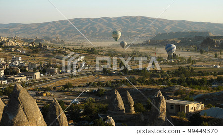 Colourful balloons fly over the mountainous landscape of Cappadocia. A popular tourist spot. Hot air balloons at dawn. Colourful balloons fly over the mountainous landscape of Cappadocia. A popular tourist spot. Hot air balloons at dawn. 99449370