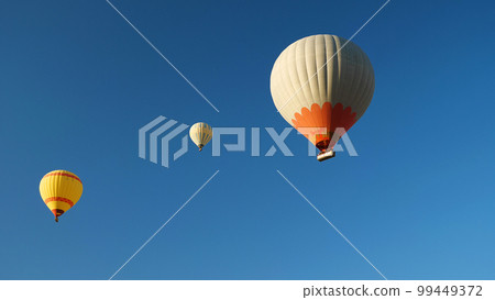Three hot air balloons with tourists against a blue cloudless sky. Beautiful view of colourful hot air balloons from below. 99449372