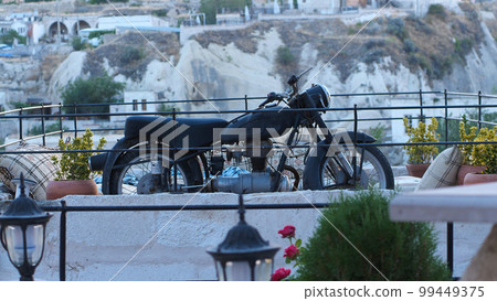 Old black motorcycle parked in front of the house. A retro motorbike against a backdrop of stone buildings and mountains. Old black motorcycle parked in front of the house. A retro motorbike against a backdrop of stone buildings and mountains. 99449375