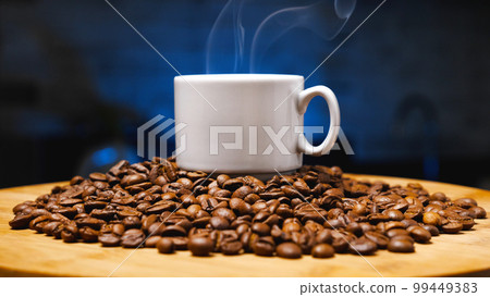 White ceramic mug and roasted coffee beans on a wooden base. Close up. Dark blue background. Concept of a coffee shop. Coffee as a way of life for the modern man. White ceramic mug and roasted coffee beans on a wooden base. Close up. Dark blue background. Concept of a coffee shop. Coffee as a way of life for the modern man. 99449383