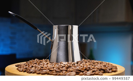 A pile of roasted brown coffee beans and a steel cezve. Turkish coffee. Coffee shop concept. Dark blue background. A pile of roasted brown coffee beans and a steel cezve. Turkish coffee. Coffee shop concept. Dark blue background. 99449387
