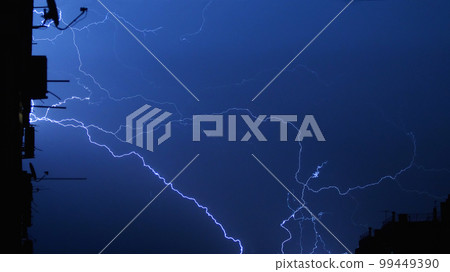 Lightning in the city night sky, bright flashes in the clouds during thunderstorms. Several flashes of lightning at night against the background of a multi-storey building. Lightning in the city night sky, bright flashes in the clouds during thunderstorms. Several flashes of lightning at night against the background of a multi-storey building. 99449390