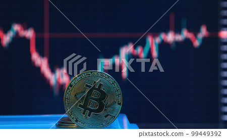 Bitcoin coin in front of a screen with a skewed graph of the cryptocurrency's value. Cryptocurrency crisis. BTC coin close-up. 99449392