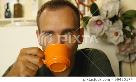 In a coffee shop, a middle-aged man is enjoying a hot cup of coffee. A man is drinking coffee from an orange mug. In a coffee shop, a middle-aged man is enjoying a hot cup of coffee. A man is drinking coffee from an orange mug. 99450174