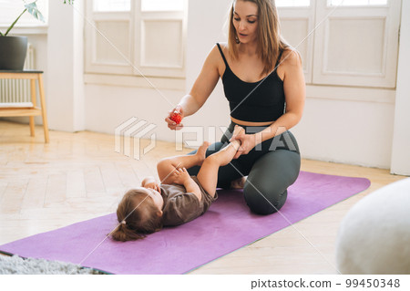 Young woman fit mom with baby girl doing exercises with massage ball on mat at home Young woman fit mom with baby girl doing exercises with massage ball on mat at home 99450348