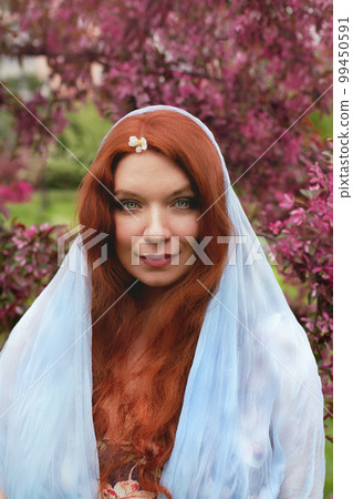 redhead young woman with green eyes and freckles wearing blue cape with cherry flowerm on her forehead in rose cherry blossom redhead young woman with green eyes and freckles wearing blue cape with cherry flowerm on her forehead in rose cherry blossom 99450591