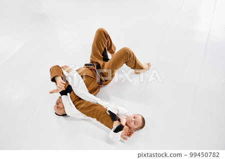 Top view. Dynamic portrait of man, professional judo, jiu-jitsu coach training with little boy, child in white kimono. Sportive hobby 99450782