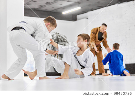 Professional sport activity. Boys, children in white kimono training, practising judo, jiu-jitsu exercises indoors 99450786