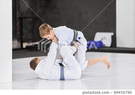 Boys, children in white kimono training, practising judo, jiu-jitsu exercises indoors. Growing strength, sportive kowledges 99450790
