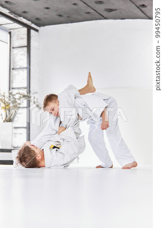 Professional exercises. Boys, children in white kimono training, practising judo, jiu-jitsu exercises indoors Professional exercises. Boys, children in white kimono training, practising judo, jiu-jitsu exercises indoors 99450795