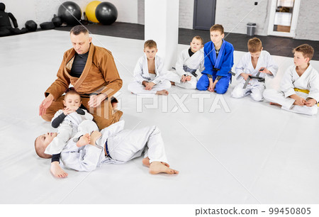 Boys, children in white kimono training judo, jiu-jitsu fight style indoors with coach. Developing strength and endurance Boys, children in white kimono training judo, jiu-jitsu fight style indoors with coach. Developing strength and endurance 99450805