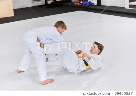 Two boys, children in white kimono training judo, jiu-jitsu fight style indoors. Developing strength and sportive knowledges 99450827