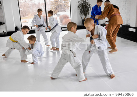 Little boys, children in white kimono training judo, jiu-jitsu sport activity indoors with professional coach Little boys, children in white kimono training judo, jiu-jitsu sport activity indoors with professional coach 99450866