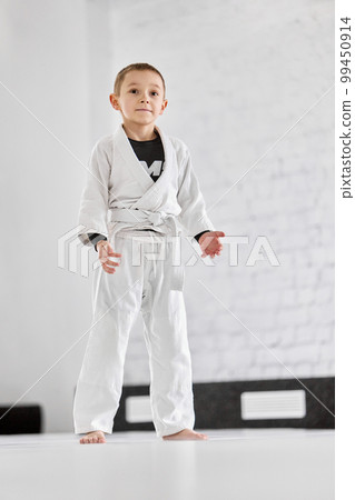 Portrait of little boy, child in white kimono attending sport class, training judo, jiu-jitsu in gym. Sportive active kid Portrait of little boy, child in white kimono attending sport class, training judo, jiu-jitsu in gym. Sportive active kid 99450914