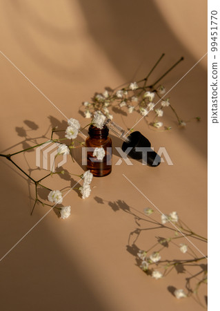 Small bottle of serum on neutral beige background. Beauty pipette dropper with Gypsophila or baby's breath white flowers. Glass dropper of cosmetic oil and dried flowers and herbs. Natural organic Small bottle of serum on neutral beige background. Beauty pipette dropper with Gypsophila or baby's breath white flowers. Glass dropper of cosmetic oil and dried flowers and herbs. Natural organic 99451770