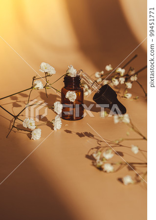 Small bottle of serum on neutral beige background. Beauty pipette dropper with Gypsophila or baby's breath white flowers. Glass dropper of cosmetic oil and dried flowers and herbs. Natural organic Small bottle of serum on neutral beige background. Beauty pipette dropper with Gypsophila or baby's breath white flowers. Glass dropper of cosmetic oil and dried flowers and herbs. Natural organic 99451771