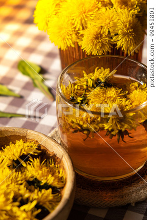Dandelion flower healthy tea in glass cup on table. Herbal medicine Delicious tisane tea from with fresh yellow blossom dandelion flowers inside tea cup. Green clearing infusion Wildflowers Eco Dandelion flower healthy tea in glass cup on table. Herbal medicine Delicious tisane tea from with fresh yellow blossom dandelion flowers inside tea cup. Green clearing infusion Wildflowers Eco 99451801