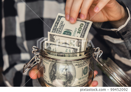 Dollar banknote saving money in glass jar. Unrecognizable woman moderate consumption and economy Collecting money. Tips. Business, finance, saving, banking and people concept. Extra money, passive 99452092