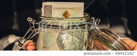 Polish zloty banknote saving money in glass jar. Unrecognizable woman moderate consumption and economy Banner Collecting money. Tips. Business, finance, saving, banking and people concept. Extra 99452102