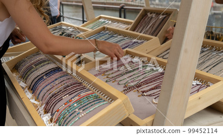Jewelery showcase on street market. Woman choosing decorations on local street market in Gdansk, Poland. Female tourist is choosing souvenirs in street shop and looking at color bracelets. Candid 99452114