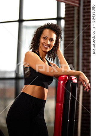Slender athletic African American woman in sportswear smiling at the camera in a good mood between workouts in the gym. 99452390