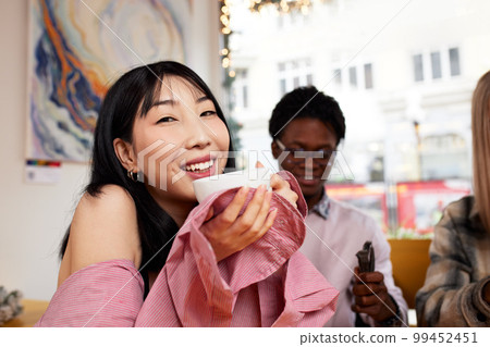 Multiracial happy young people, black and white cheerful comrades laughing, enjoying food, having fun sitting together at a table in a restaurant, different friends sharing lunch at a meeting Multiracial happy young people, black and white cheerful comrades laughing, enjoying food, having fun sitting together at a table in a restaurant, different friends sharing lunch at a meeting 99452451