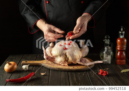 Cooking chicken in the kitchen with the hands of a chef. Before baking, the cook adds red viburnum to raw chicken. Asian cuisine 99452518