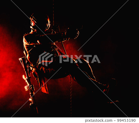 Silhouette of police officer in tactical gear descending from a height, rope exercises with weapons. Tactical rappelling, anti-terror or counter terrorism operation in darkness in rappelling harness 99453190