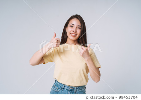 Young happy asian woman winner with long hair in yellow shirt and jeans on grey background Young happy asian woman winner with long hair in yellow shirt and jeans on grey background 99453704