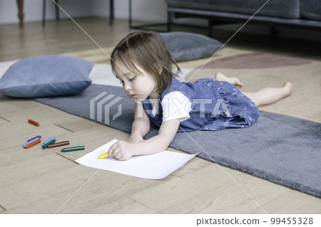 A two-year-old girl lies on the floor and draws with pencils. A two-year-old girl lies on the floor and draws with pencils. 99455328