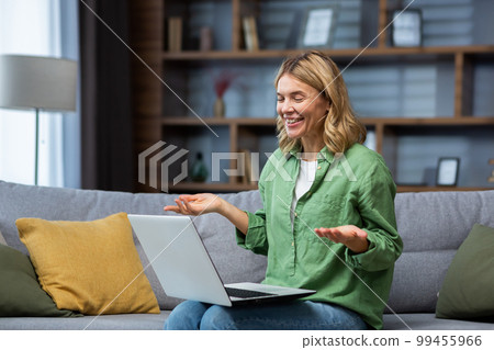 Cheerful and happy mature woman alone at home sitting on sofa in living room and using laptop for video call, housewife smiling and talking with friends remotely. Cheerful and happy mature woman alone at home sitting on sofa in living room and using laptop for video call, housewife smiling and talking with friends remotely. 99455966