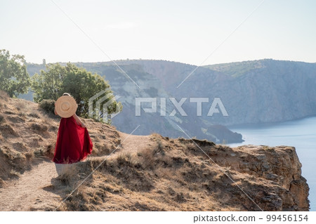 A woman in a red flying dress fluttering in the wind, against the backdrop of the sea. 99456154