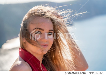 A woman in a red flying dress fluttering in the wind, against the backdrop of the sea. 99456165