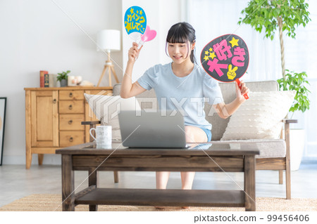 Oshikatsu A girl from the z generation who cheers for her favorite by waving a fan while watching a live video 99456406