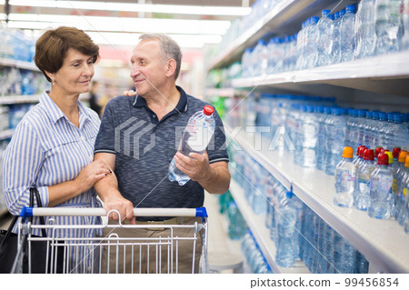 Mature couple husband and wife choose bottle of drinking water in supermarket 99456854