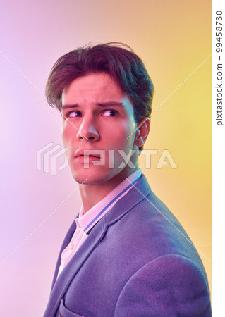 One young Caucasian man, student graduate in jacket posing isolated over light gradient yellow-purple background in neon light. Fashion, art, education, business concept 99458730