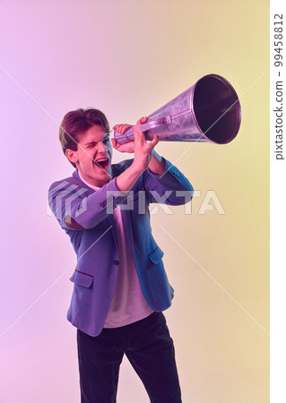 Portrait of young man looking at retro megaphone isolated over light background in neon light. Concept of emotions, facial expression, lifestyle, fashion, youth culture 99458812