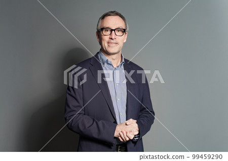 Portrait of happy smiling mature businessman in blue suit and glasses against grey wall background 99459290