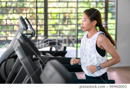 young happy asian woman athlete run on treadmill, running machine, in indoor gym fitness for health; 99460001
