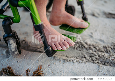 Close-up of mens feet on wheelchair, on beach. Close-up of mens feet on wheelchair, on beach. 99460098