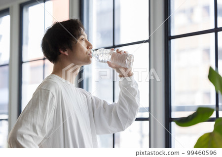 A man drinking bottled water by the window A man drinking bottled water by the window 99460596