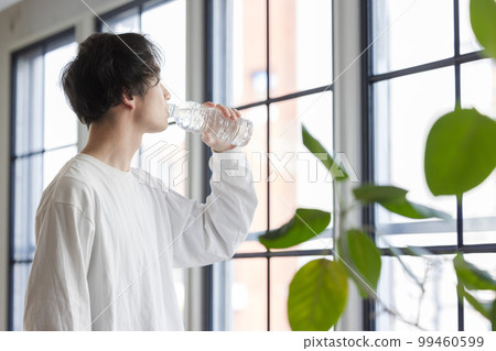 A man drinking bottled water by the window 99460599