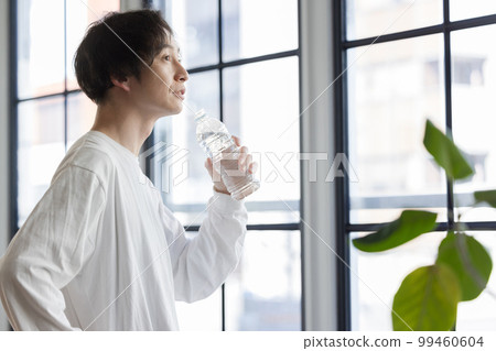 A man drinking bottled water by the window 99460604