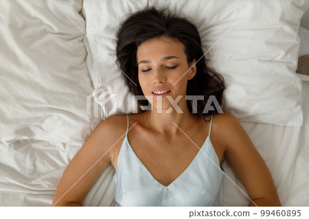 Spanish young woman dressing nightie lying on bed in bedroom. Overhead top view 99460895